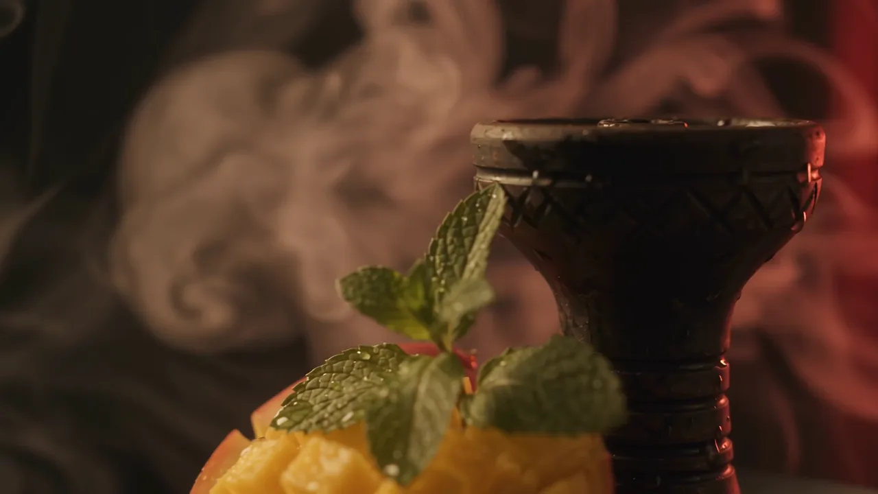 Cut mango and mint beside a hookah bowl in smoke