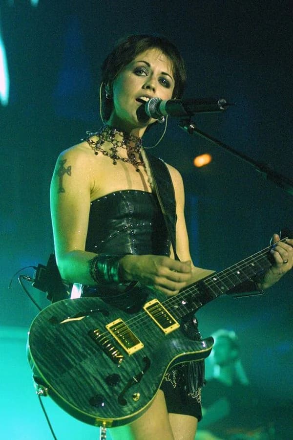 Dolores O'Riordan singing into a microphone on stage while playing an electric guitar