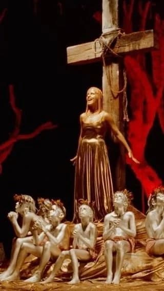 A still from the Zombie video: Dolores painted gold, standing in front of a large cross with boys painted silver sitting at her feet